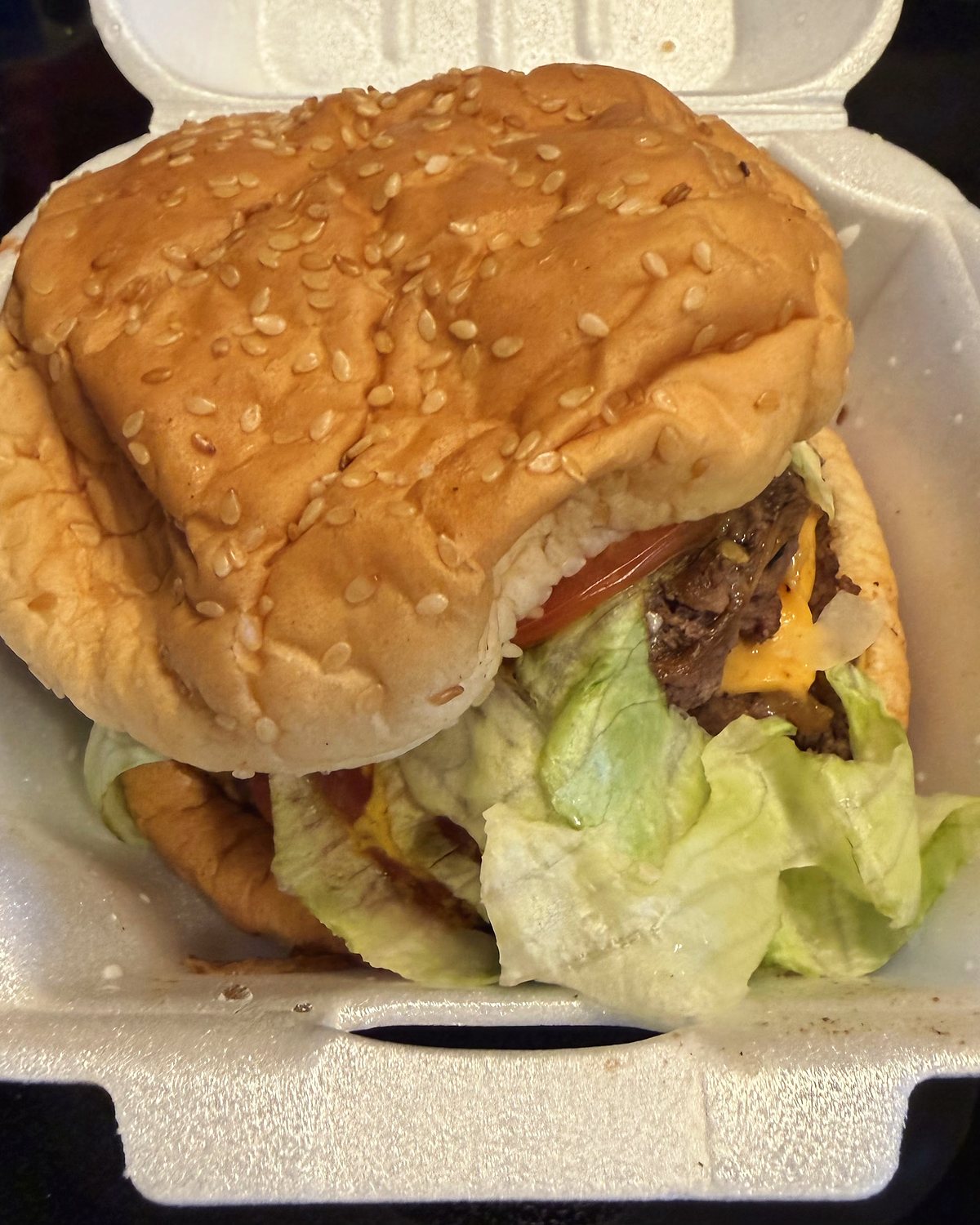 A large double cheeseburger with lettuce and tomato in a takeout container.