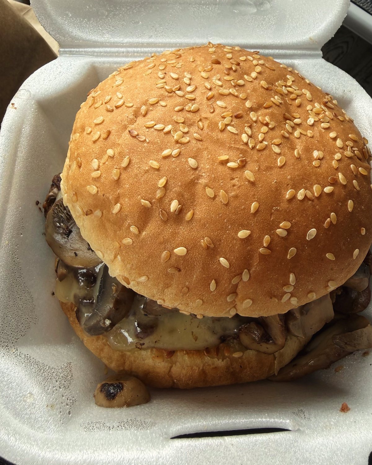A mushroom and Swiss burger on a sesame bun in a takeout container.