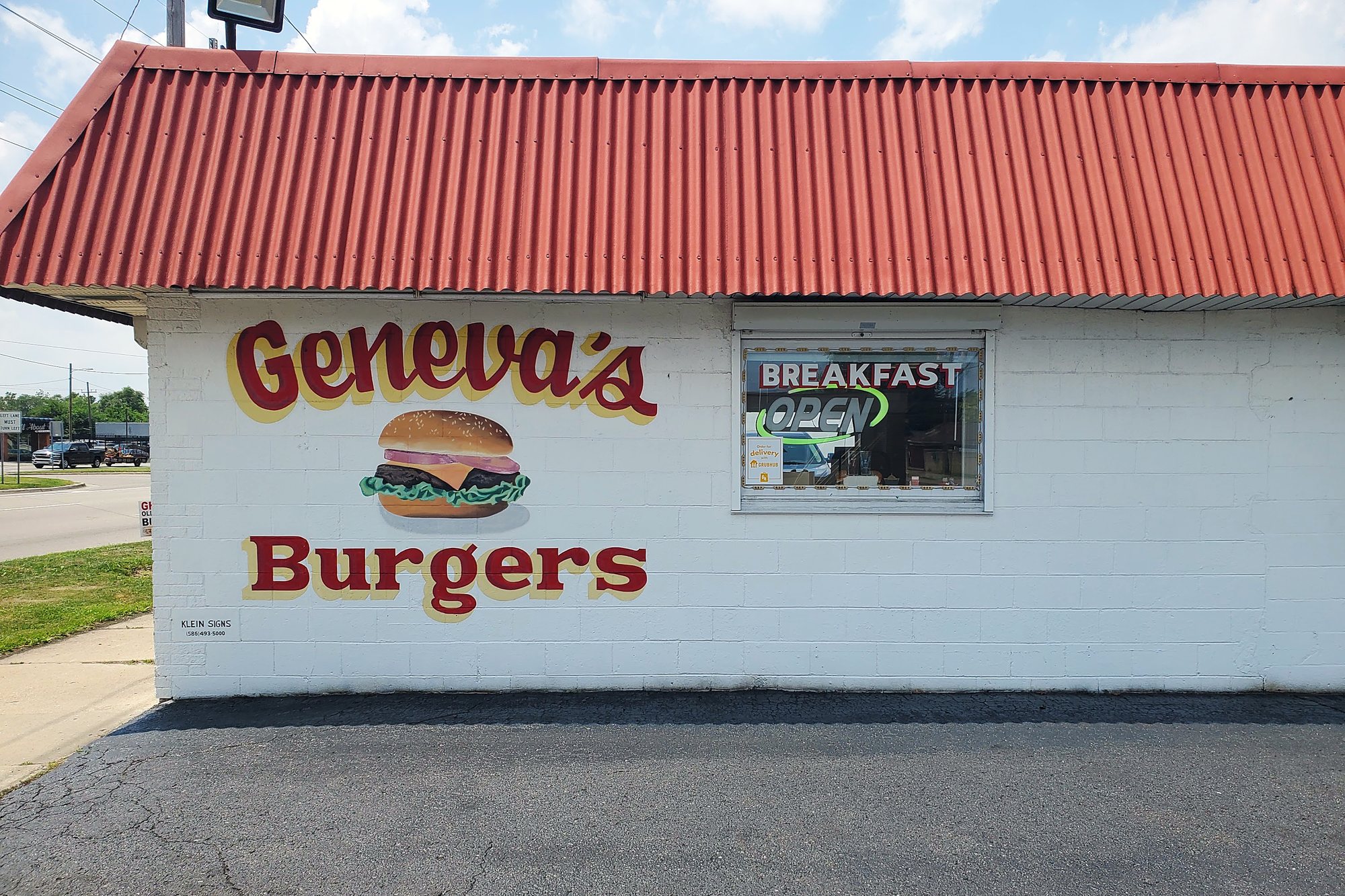The side of Geneva's Burgers, white block wall with the name hand painted in red beside a painted burger.